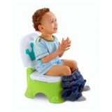 Niño o niña sentado en el orinal interactivo verde con corona azul durante el aprendizaje